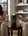 The Strawberry Shop black brick water candle with warm LED light on a side table in a cozy living room setting.