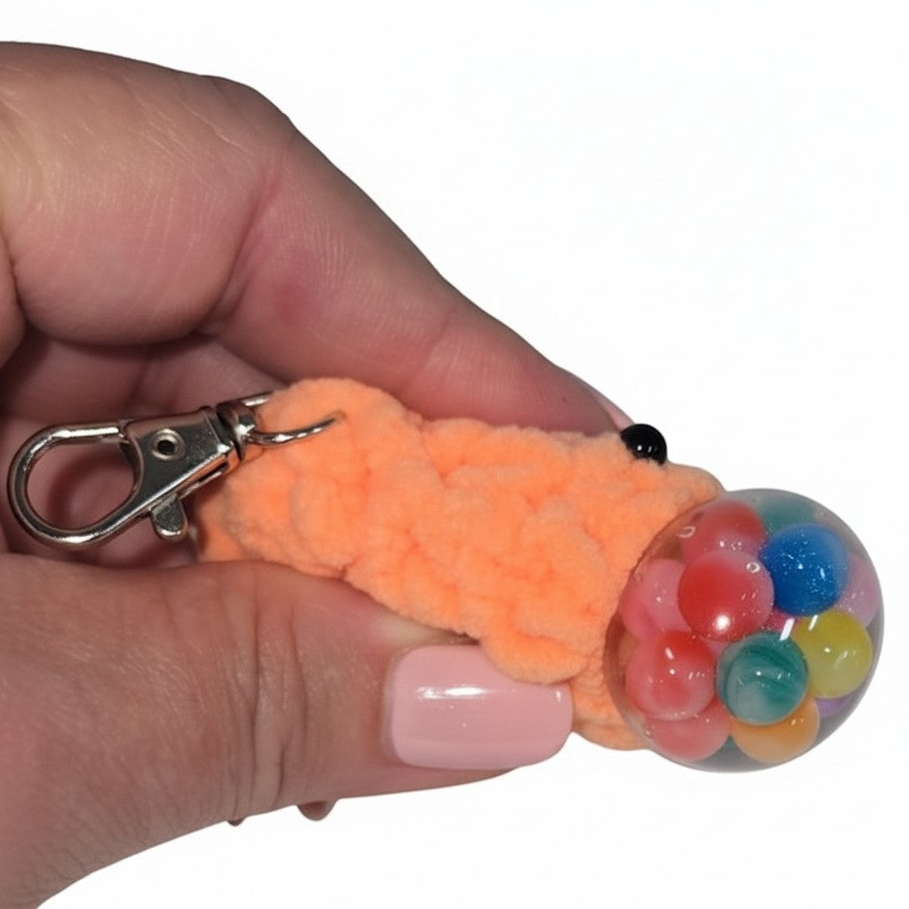 The Strawberry Shop orange crochet blob keychain with googly eyes and a clear squishy ball filled with colorful beads.