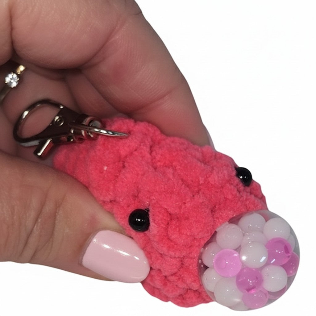 The Strawberry Shop handmade pink crochet blob keychain with bead eyes and a clear sphere filled with pink beads.