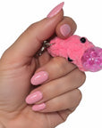 The Strawberry Shop pink crocheted blob stress ball keychain with bead eyes held in a hand with matching pink nails.